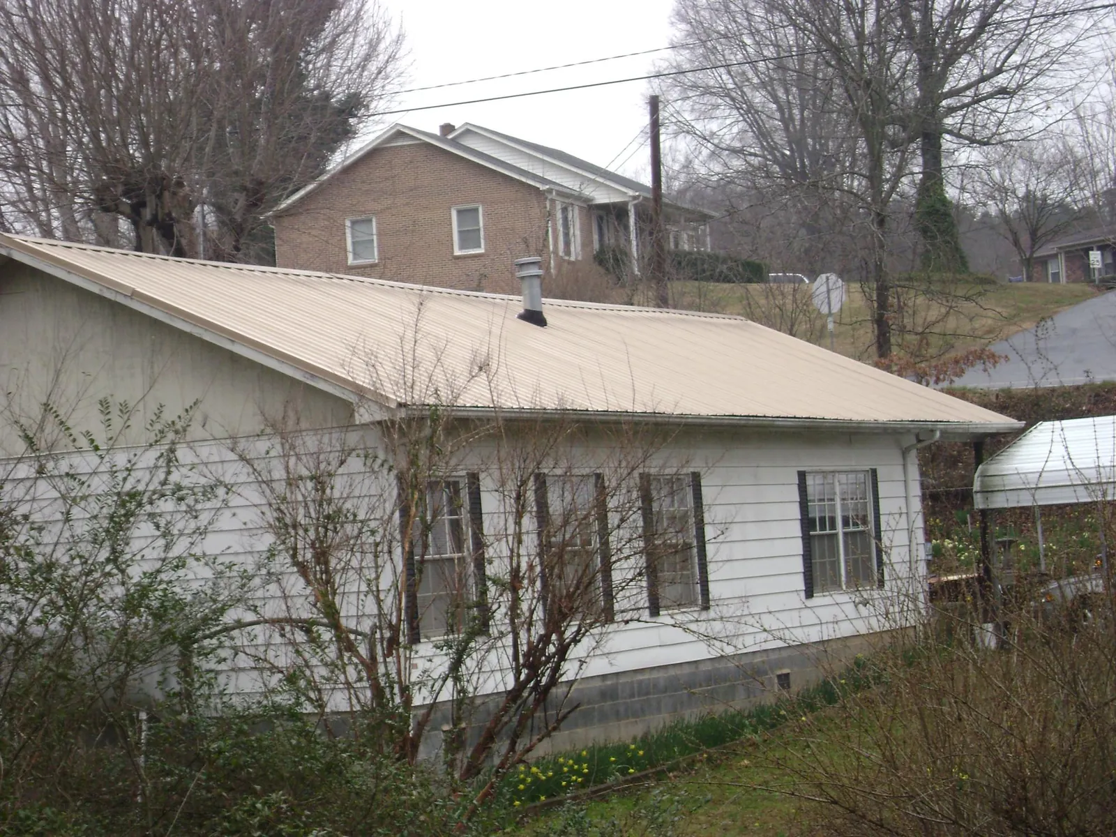Tan metal roof on a white sided house set into a hillside — Commercial Roofing by Roofing Brothers in De Soto