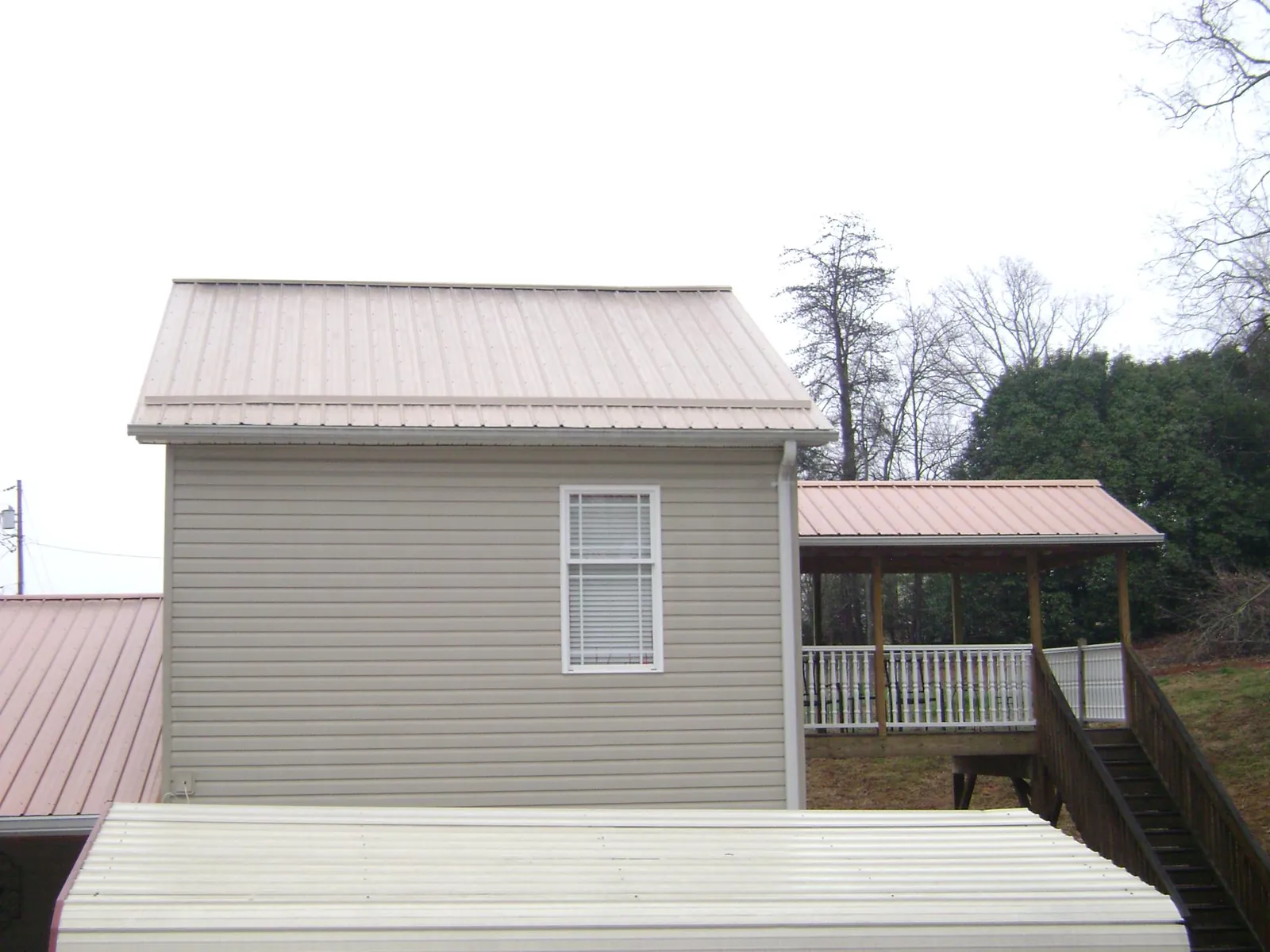 Tan metal roofs on a two story addition and attached porch, from a Roof Replacement job in De Soto
